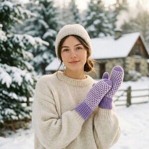 May include: A person wearing a cream-colored knit hat and sweater, holding purple and white patterned mittens. The background features a snowy landscape with trees and a house, suggesting a winter theme.