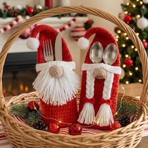 May include: Two red crocheted gnome-shaped cutlery holders sit inside a woven wicker basket. One gnome features a white yarn beard and holds a silver fork and knife, while the other has white braided yarn hair and holds two silver spoons.