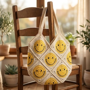May include: A cream-colored crochet tote bag featuring a repeating pattern of yellow smiley face squares. The bag has two matching crochet handles and is constructed from multiple diamond-shaped panels stitched together in a grid formation.