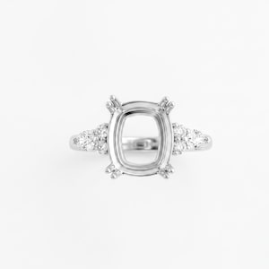 May include: A silver ring setting with a cushion-shaped center and small accent stones on each side. The ring is set against a white background, highlighting its intricate design and potential for customization.
