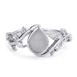 May include: A silver ring featuring a teardrop-shaped setting, framed by a detailed vine motif with leaves and small, clear gemstones. The ring has a polished finish and a nature-inspired design.