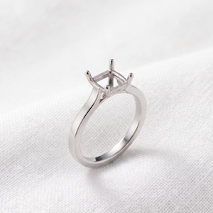 May include: A silver-toned metal ring setting featuring a four-prong head designed to hold a square-shaped gemstone. The band is smooth and polished, with a simple, clean structure that tapers slightly as it reaches the prong setting at the top.
