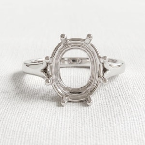 Peut inclure: Une monture de bague en métal argenté brillant dotée d'un support central ovale destiné à recevoir une pierre précieuse. L'anneau est lisse et plein, avec six griffes s'étendant vers le haut depuis la base ovale pour fixer la pierre.