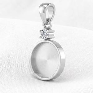 May include: A silver-toned metal pendant setting featuring a circular, flat-bottomed bezel cup designed for inlay. The pendant includes a single, clear, round-cut faceted stone set in a six-prong mount positioned directly above the circular bezel.