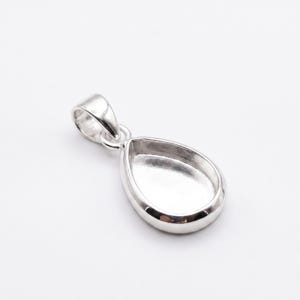 May include: A silver pendant with a teardrop-shaped bezel. The pendant has a loop at the top for a chain and a recessed area to hold a stone or other decorative element. The metal has a polished finish.