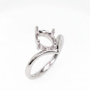 Peut inclure: Une monture de bague en métal argenté poli avec un anneau en forme de V et un panier ovale à quatre griffes conçu pour accueillir une pierre précieuse. La surface métallique est lisse et réfléchissante, offrant une structure épurée.