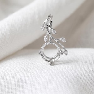 May include: A silver-toned metal pendant setting featuring a circular center mount for a gemstone. The design includes a curved branch-like stem extending upward, adorned with five small, clear, round-cut stones set along the delicate metal vine.