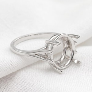 Peut inclure: Une monture de bague en métal argenté poli dotée d'une tête circulaire avec plusieurs griffes conçues pour maintenir une pierre précieuse. L'anneau présente un design à tige fendue qui s'affine vers le haut, rejoignant la structure centrale.
