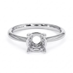 May include: A silver ring with a round setting designed to hold a gemstone. The ring has a polished, smooth band that tapers towards the setting. The setting features four prongs to secure the stone. The ring is displayed on a white background.