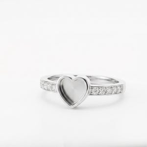 Könnte beinhalten: Ein silberner Ring mit herzförmiger Fassung. Das Band ist mit kleinen, klaren Edelsteinen besetzt. Der Ring ist vor einem weißen Hintergrund platziert, der sein Design hervorhebt. Ein Schmuckstück.