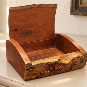 May include: A wooden box with an open lid, featuring a smooth, reddish-brown interior and a natural, rough-textured live edge on the front panel. The sides and lid are crafted from polished wood, showcasing a distinct grain pattern throughout.