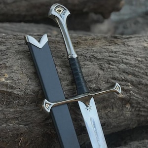 May include: A silver sword with a black handle and a black sheath. The sword has a star design on the blade and decorative accents on the hilt and crossguard. The sheath is open, revealing the blade.