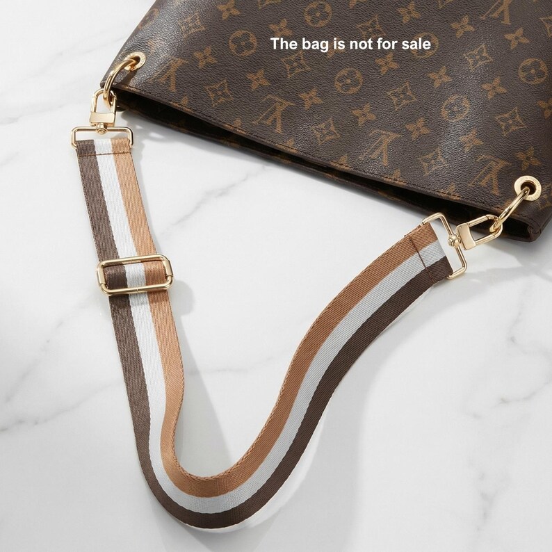 Peut inclure: Sac &agrave; main marron avec une bandouli&egrave;re ray&eacute;e. La bandouli&egrave;re pr&eacute;sente des rayures marron, blanches et beiges. Le sac est marron avec un motif r&eacute;p&eacute;titif. Le texte "The bag is not for sale" est visible.