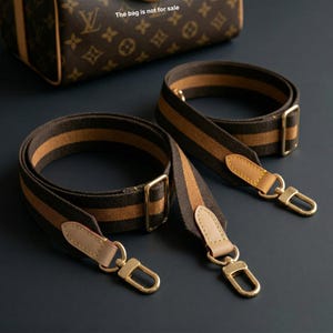 May include: Two brown and tan striped purse straps with gold-coloured hardware. The straps have leather accents and swivel clasps. A brown patterned bag is in the background. The text "The bag is not for sale" is visible.