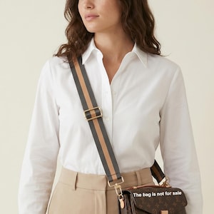 Peut inclure: Un sac &agrave; bandouli&egrave;re avec une sangle ray&eacute;e grise, beige et marron. Le sac a un ext&eacute;rieur en cuir marron avec un motif r&eacute;p&eacute;titif. La sangle est fix&eacute;e avec du mat&eacute;riel m&eacute;tallique dor&eacute;. Le texte sur le sac dit "The bag is not for sale."