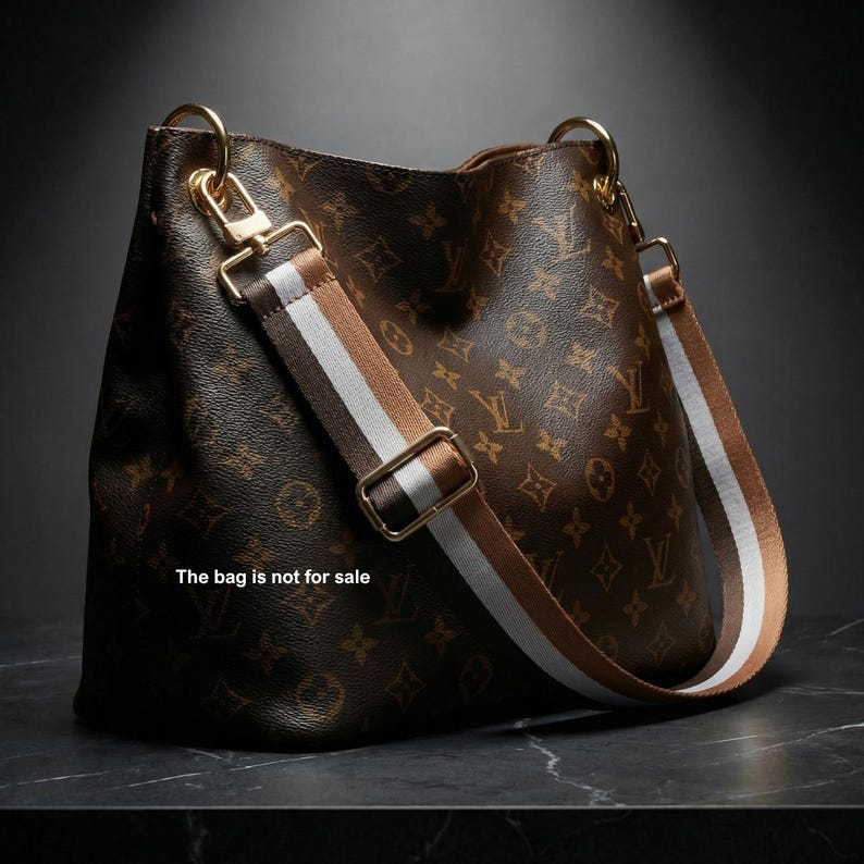 Peut inclure: Sac &agrave; bandouli&egrave;re en cuir marron avec un motif monogramme et une bandouli&egrave;re ray&eacute;e. Le sac a une quincaillerie dor&eacute;e et le texte "The bag is not for sale".