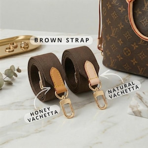 Op de afbeelding: Twee bruine canvas tasriemen met honing- en natuurlijk vachetta lederen accenten en goudkleurige hardware. De riemen zijn opgerold en tonen hun textuur en ontwerp. De tekst "BROWN STRAP" is zichtbaar.