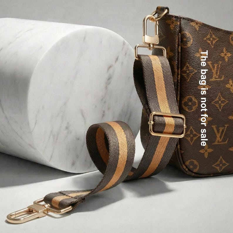Peut inclure: Sac &agrave; main marron avec un motif et une bandouli&egrave;re amovible. La bandouli&egrave;re est marron avec des rayures dor&eacute;es et une quincaillerie en m&eacute;tal dor&eacute;. Le texte sur le sac indique "The bag is not for sale".