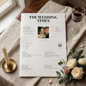 Può includere: Un giornale di nozze intitolato "THE WEDDING TIMES" con una foto di una coppia, un programma e del testo. Un bicchiere di vino rosso, una candela in un portacandele dorato e dei fiori sono su una superficie di lino.