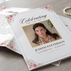 May include: A funeral program featuring a portrait of Judith Patterson, born October 12, 1945, and died May 24, 2026. The white card has a gold-bordered photo, black text reading Celebrating The Life Of, and pink floral corner illustrations.