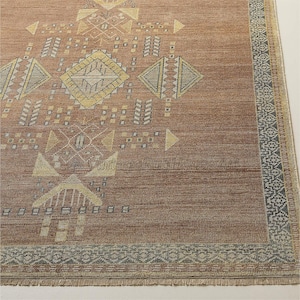 Peut inclure: Un tapis rectangulaire de couleur rouille avec un motif géométrique. Le motif présente des formes de losanges, de triangles et de rectangles dans des tons de jaune, de gris et de blanc. La bordure présente un motif répétitif gris et blanc.