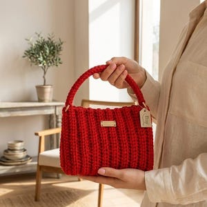 Könnte beinhalten: Eine leuchtend rote, handgehäkelte Handtasche mit einem strukturierten Rippendesign. Die Tasche hat einen abgerundeten Griff und ein kleines, rechteckiges, goldfarbenes Etikett. Ein kleines Etikett mit dem Wort "Etsy" ist am Griff befestigt.