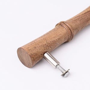 May include: A cylindrical wooden handle with a natural brown grain and a raised ring detail. A silver-toned metal mounting post with a threaded screw and a small flat washer extends from the side of the handle for attachment purposes.