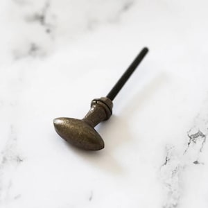 May include: A bronze cabinet knob with an oval handle and a black threaded screw. The knob is set against a white marble background, showcasing its antique aesthetic. Suitable for furniture restoration or adding a vintage touch.