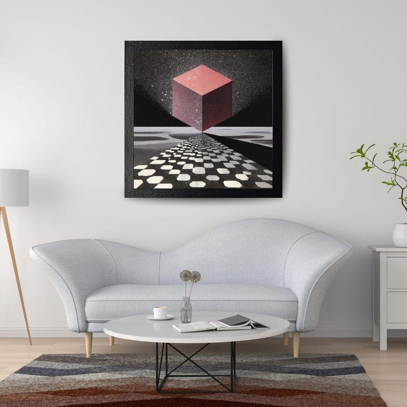 Pode incluir: Obra de arte emoldurada com um cubo vermelho suspenso sobre um caminho quadriculado em preto e branco. O fundo &eacute; um c&eacute;u estrelado. A obra est&aacute; exposta acima de um sof&aacute; cinza e de uma mesa de centro redonda.