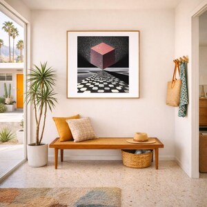 Pode incluir: Uma cena de sala de estar com uma obra de arte emoldurada que retrata um cubo geom&eacute;trico. Abaixo, um banco de madeira com almofadas e uma cesta de vime. Uma planta em vaso e um tapete completam a decora&ccedil;&atilde;o. Um chap&eacute;u de palha repousa no banco.