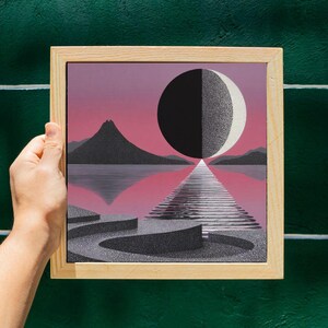 K&ouml;nnte beinhalten: Ein gerahmter Druck mit einer surrealen Landschaft mit rosa Himmel, Bergen und einem reflektierenden See. Eine gro&szlig;e schwarz-wei&szlig;e Kugel schwebt &uuml;ber einem Weg. Das Kunstwerk befindet sich in einem hellen Holzrahmen.
