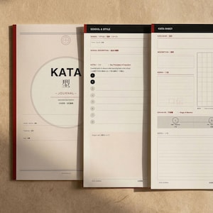May include: A set of three journals with white pages and red and black accents. The journal on the left has the word "KATA" in large letters, with Japanese characters below. The other two journals have detailed forms and charts.