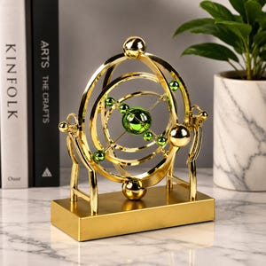 Könnte beinhalten: Eine goldfarbene, kinetische Skulptur mit konzentrischen Ringen und grünen Kugeln. Die Skulptur steht auf einem rechteckigen Sockel und weist eine zentrale grüne Kugel auf. Das Design erinnert an ein Planetarium oder ein Modell des Sonnensystems.