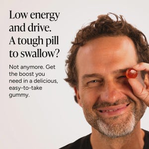 May include: A small, round, translucent orange gummy held up to the eye. The text reads: Low energy and drive. A tough pill to swallow? Not anymore. Get the boost you need in a delicious, easy-to-take gummy. The background is a plain light color.