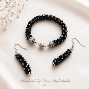 May include: A jewellery set consisting of a circular bracelet and two matching drop earrings. Each piece is crafted from small, faceted black beads and silver-toned accents. The bracelet features a magnetic clasp. Text reads: Handmade by Olena Shuliakivska.