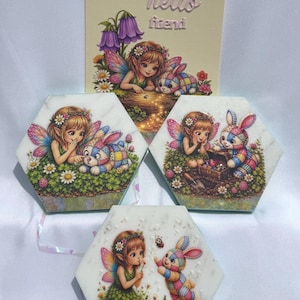May include: Three hexagonal white stone coasters and one rectangular card featuring illustrations of a fairy with wings and a patchwork rabbit. The text "hello friend" is printed on the card. The fairy wears a green leaf dress and flower crown.