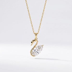 Può includere: Una collana color oro con un ciondolo a forma di cigno. Il corpo del cigno è formato da una grande pietra preziosa trasparente a taglio marquise, mentre il collo e la testa sono realizzati in metallo dorato lucido con un piccolo accento nero.