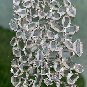 May include: A collection of numerous small, clear, double-terminated quartz crystals arranged in a dense cluster. Each individual crystal features a hexagonal prismatic shape with pointed ends, exhibiting natural transparency and geometric facets.