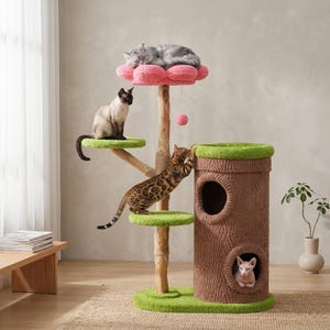 May include: A multi-level cat tree with a pink flower-shaped top, green platforms, and a brown tree trunk-shaped structure. Three cats are interacting with the cat tree. One cat is sleeping on the top, another is sitting on a platform, and a third is climbing the tree.