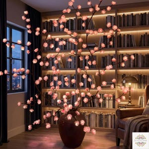 May include: A large brown vase holds a decorative lighted cherry blossom branch with pink flowers. The branches extend upwards and outwards, creating a soft glow in a room with a bookshelf and a window.