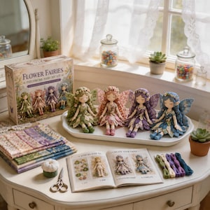 May include: A Flower Fairies patchwork fairy DIY kit box, four fabric fairy dolls in green, pink, purple, and blue, a stack of patterned fabric squares, a step-by-step instruction book, embroidery thread, and metal scissors on a table.