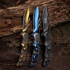 Puede incluir: Tres navajas de bolsillo personalizadas con diseños de lobos. Las hojas son doradas, azules y grises, cada una grabada con un nombre: David, Steven y Mark. Los mangos presentan tallas detalladas de lobos.