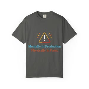 May include: Dark gray t-shirt with a graphic of a yellow, orange, and red hazard symbol and the text "Mentally In Production Physically In Panic" in blue and orange. The shirt is made of a soft material.