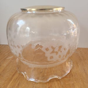 Peut inclure: Un abat-jour en verre transparent avec un capuchon en métal argenté. L'abat-jour a une forme ronde et bulbeuse avec un motif texturé et une base à volants. Le luminaire est conçu pour être monté au plafond ou au mur.