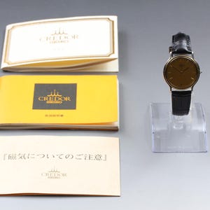 May include: A Credor Seiko wristwatch with a round gold-tone dial and a black leather strap, displayed on a clear stand. Included are three paper booklets with the Credor Seiko logo and Japanese text regarding magnetic field precautions.