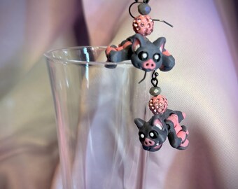 May include: A pair of dangle earrings featuring sculpted gray and pink pig figures. Each earring includes a dark metal hook, a small gray bead, and a round pink bead covered in tiny sparkling crystals, suspended above the pig charm.