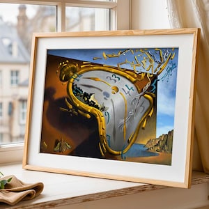 May include: A framed print of Salvador Dalí's "The Persistence of Memory" featuring a melting clock. The surrealist artwork has a light wood frame and is displayed on a windowsill. The background shows a cityscape and a white curtain.
