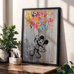 Può includere: Opera d'arte incorniciata con Topolino che tiene in mano palloncini colorati. L'opera ha uno sfondo grigio con gocce di vernice e spruzzi colorati. L'immagine è esposta su una superficie di legno con una pianta e delle matite.