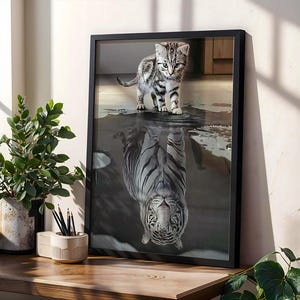 May include: Framed art print featuring a kitten standing above its reflection, which appears as a tiger. The artwork is in black and white, with the kitten in shades of gray and black. The print is displayed in a black frame.