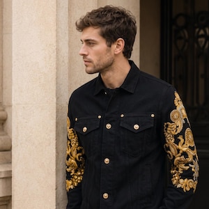 May include: Black denim jacket with gold embroidery on the sleeves, featuring a floral and scrollwork pattern. The jacket has gold-tone buttons and pocket details. A classic style.